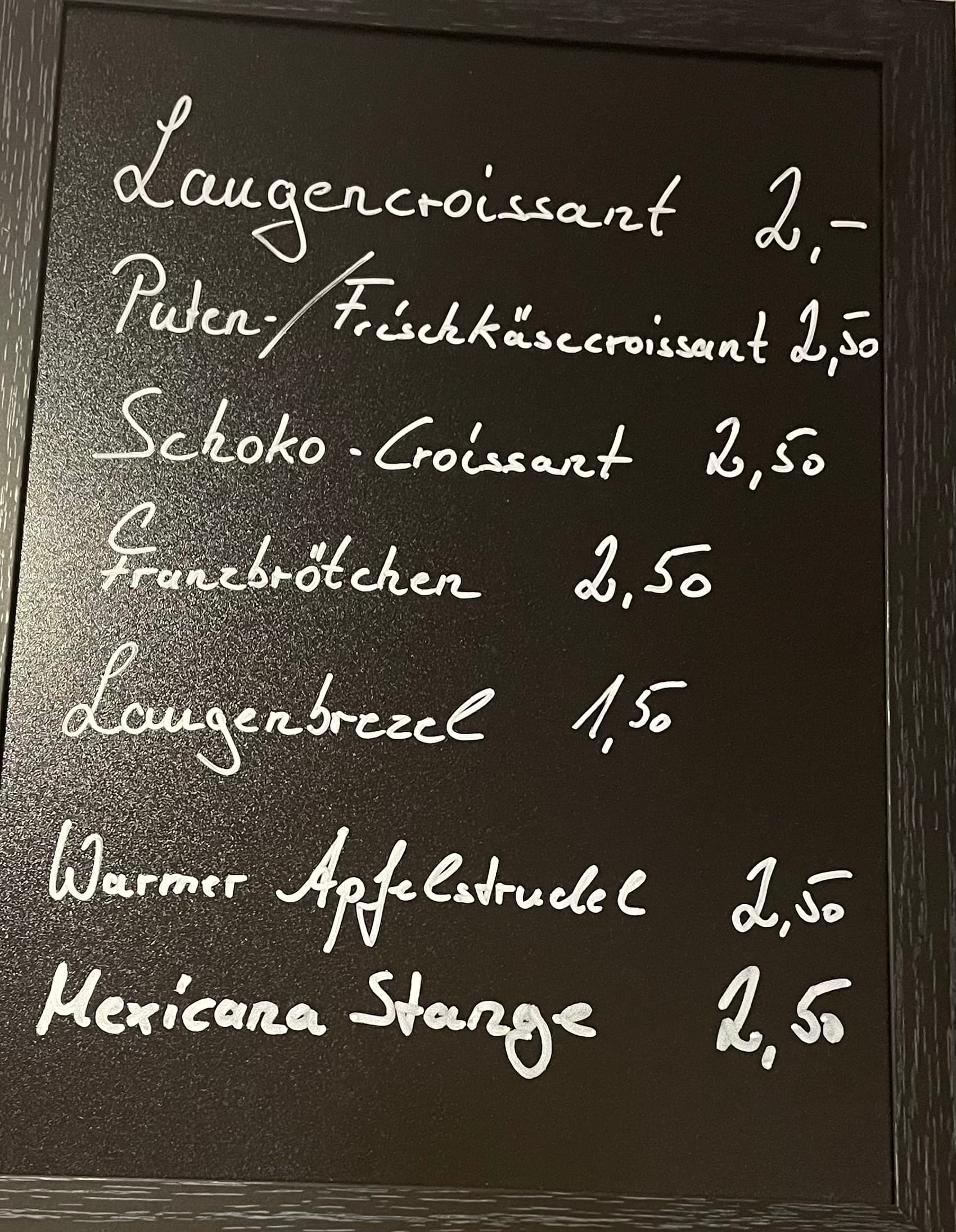 Auf einer Speisekarte in deutscher Sprache sind Backwaren und Preise aufgeführt, darunter Laugencroissant, Puten/Frischkäsecroissant, Schoko-Croissant, Franzbrötchen, Laugenbrezel, Warmer Apfelstrudel und Mexicana Stange.